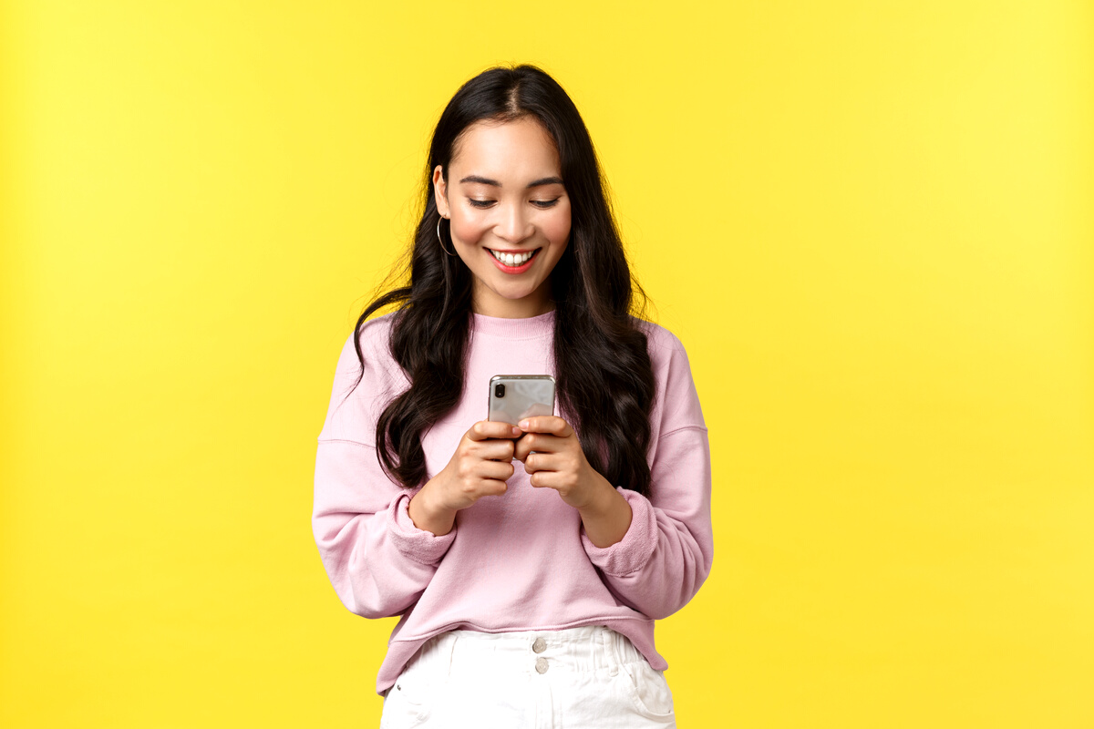 People Emotions, Lifestyle Leisure and Beauty Concept. Young Modern Asian Girl Blogger Make Post on Social Media Using Smartphone App, Messaging, Looking at Mobile Phone with Pleased Smile